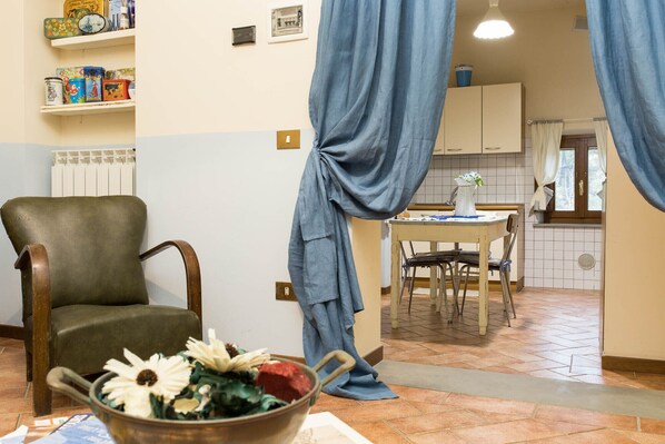Una sala de estar con un sillón verde, un comedor con mesa y sillas, y una cocina visible a través de un vano abierto.