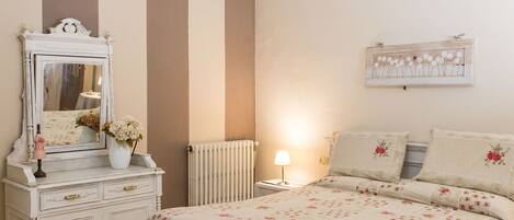 A bedroom with a bed, dresser, mirror, lamp, and floral artwork on the wall.