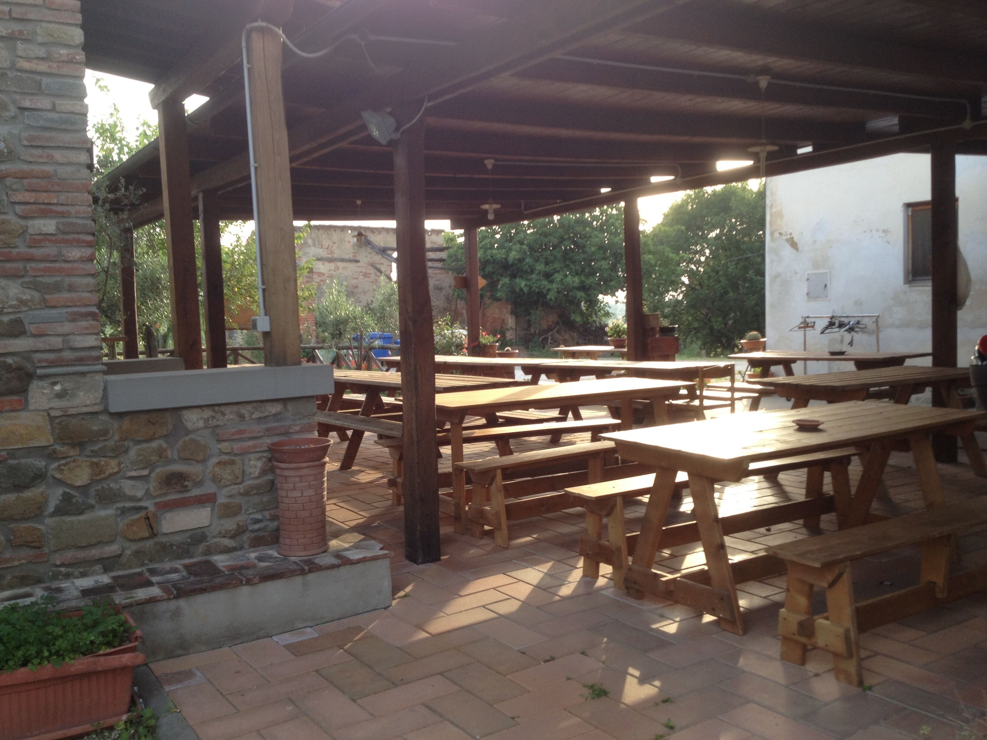 An outdoor patio with wooden tables and benches, stone walls, and a brick floor.
