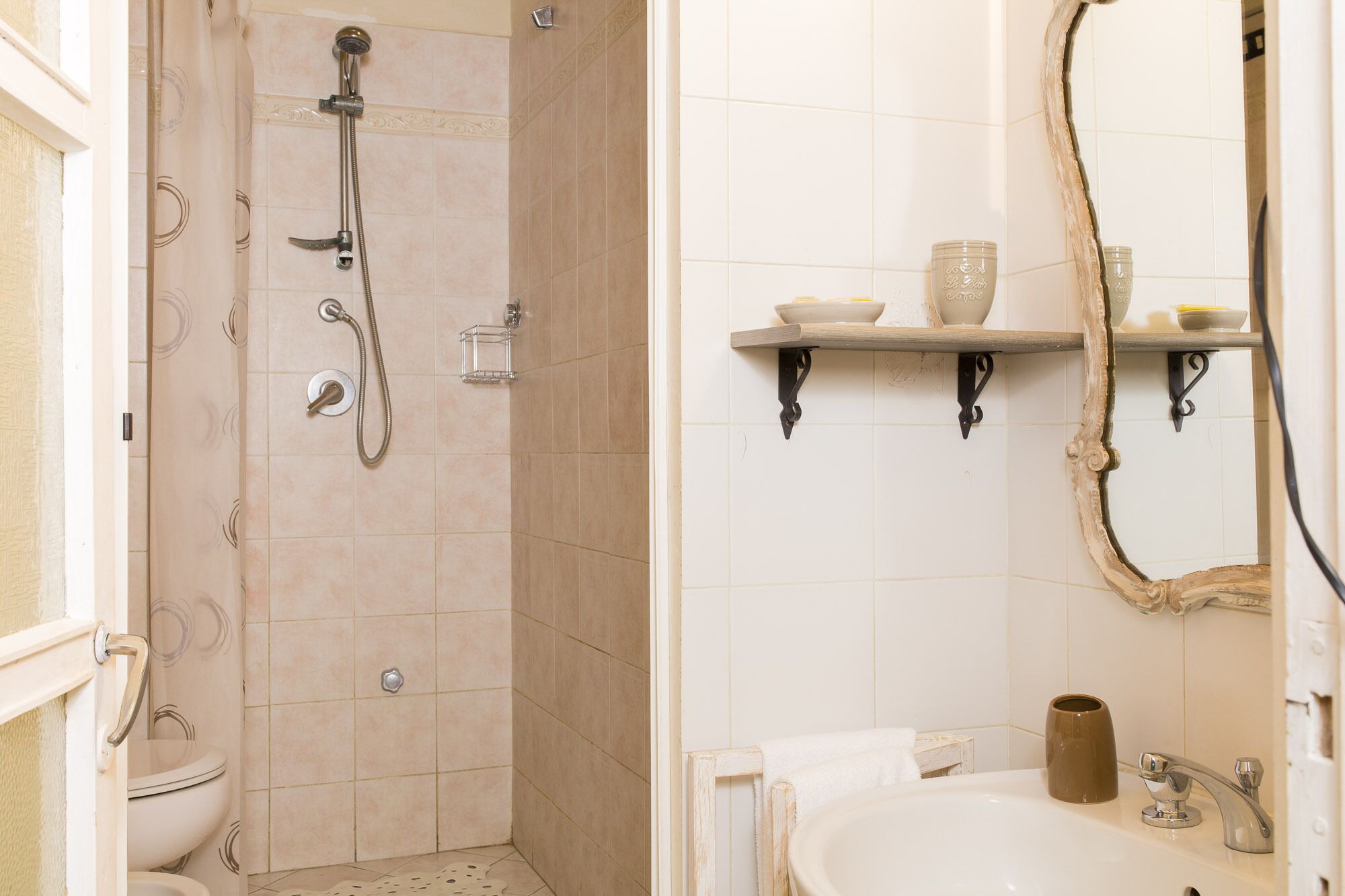 Un baño con ducha, inodoro, lavabo y un estante con artículos de aseo.