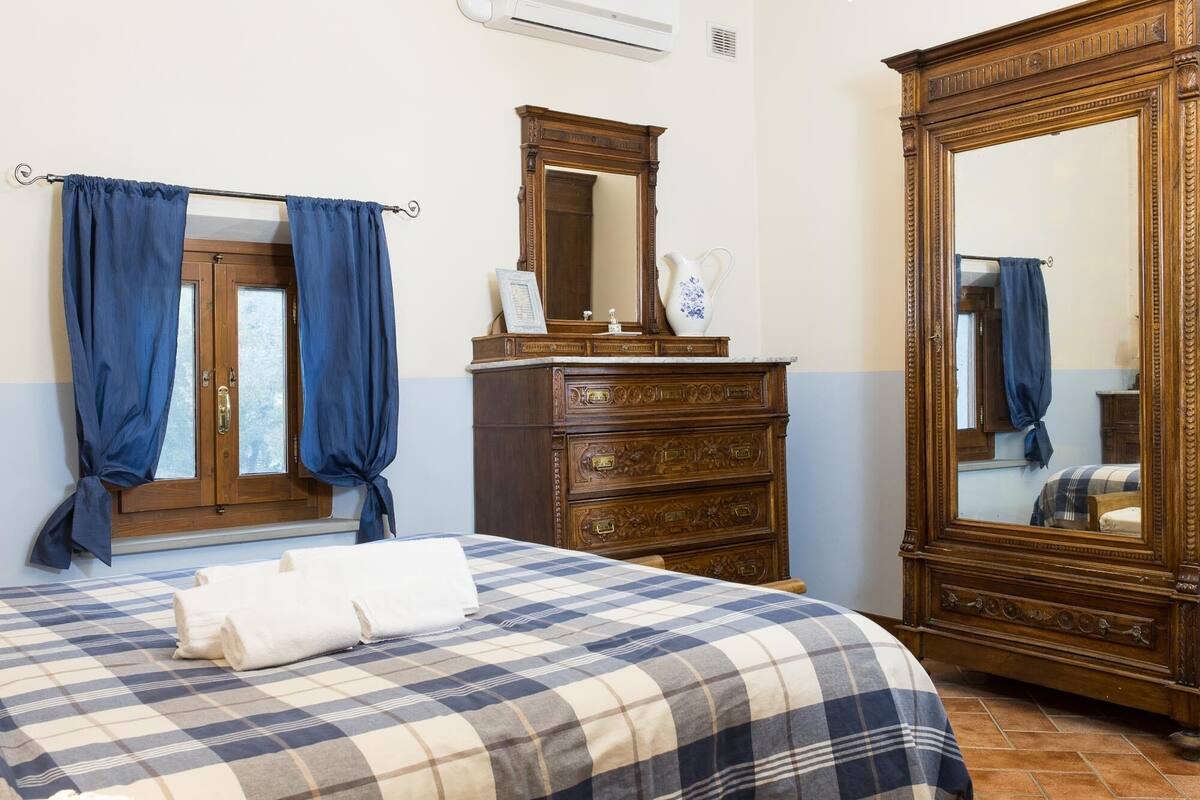 A bedroom with a bed, a wooden dresser, a mirror, and a window with curtains.