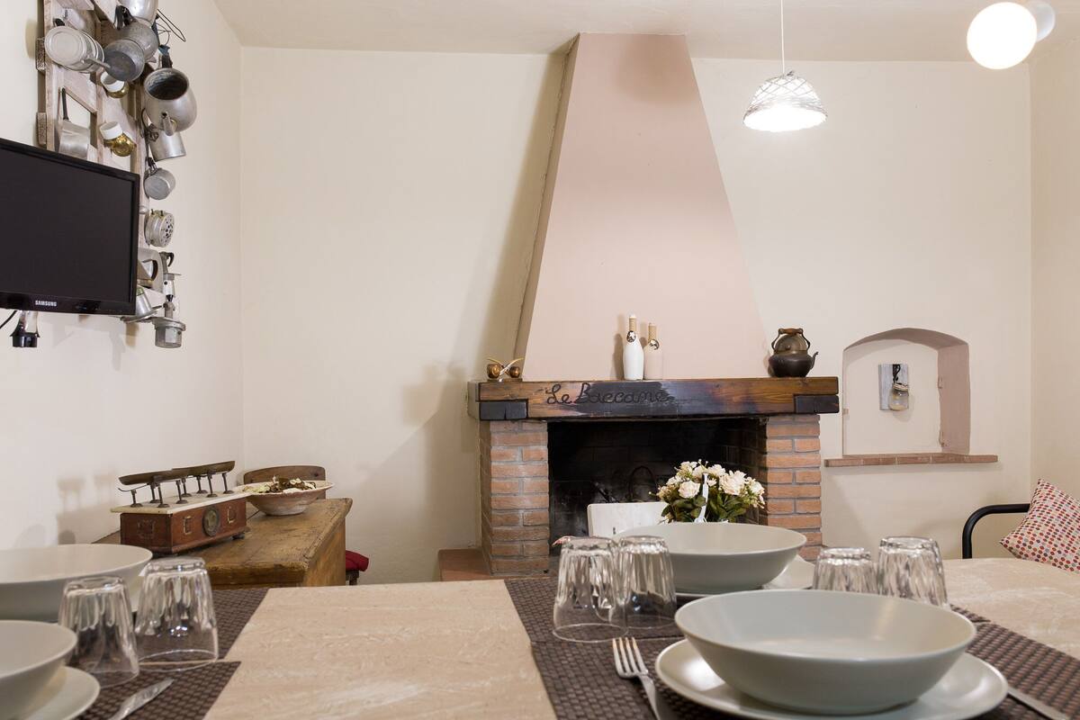 A dining area with a brick fireplace, a television mounted on a wall, and a table set for a meal.