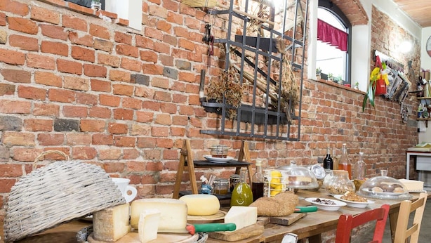 Een rustieke bakstenen muur met een houten tafel waarop verschillende kazen en brood staan.