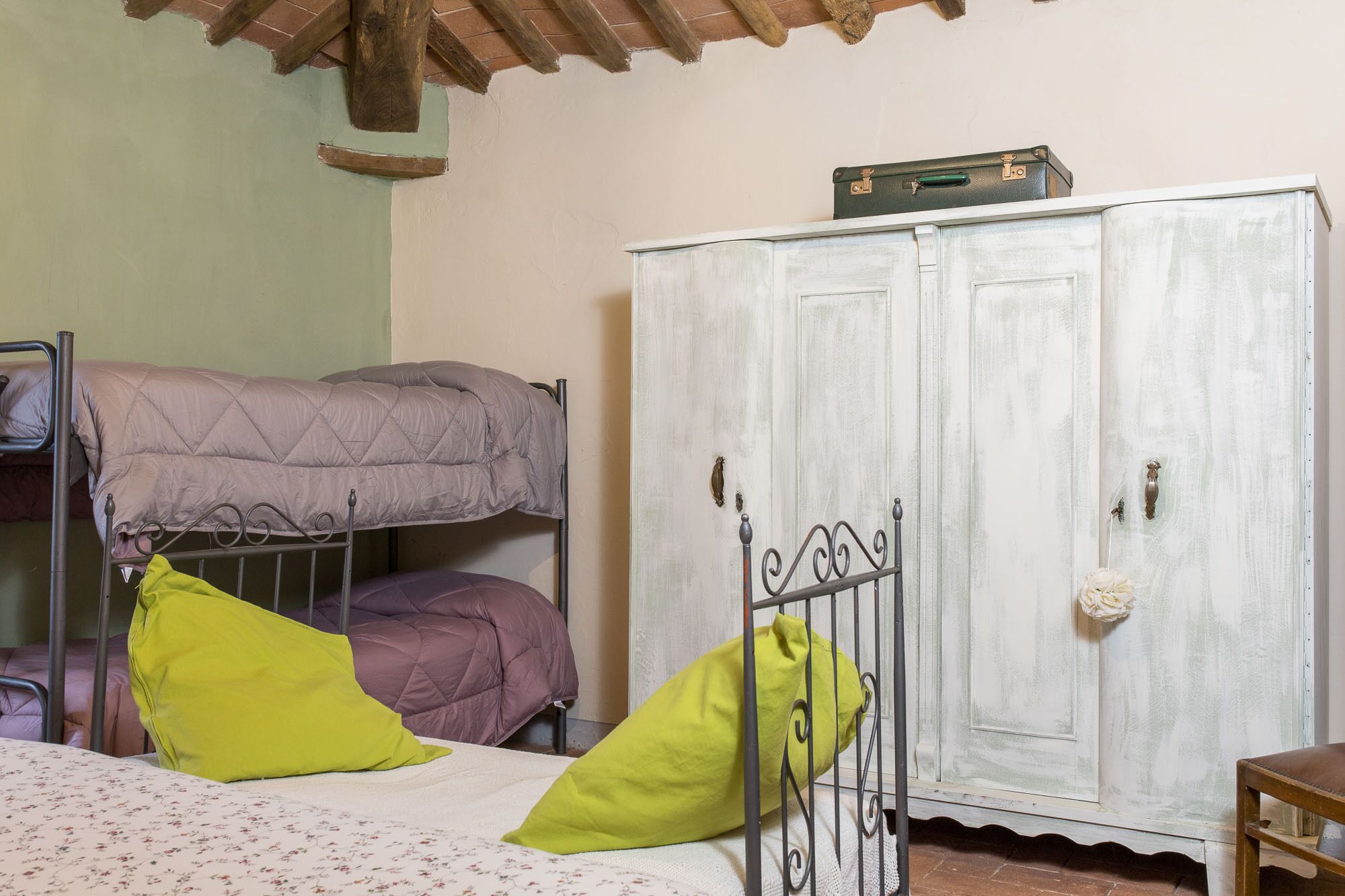 A dormitory room with bunk beds, a wardrobe, and a bed with floral bedding.