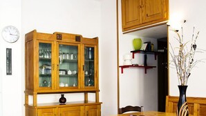 A dining area with a wooden table, chairs, a cabinet with glass doors, a ceiling fan, and a clock on the wall. - Manzoni Apartment Le Castella (Le Castella)