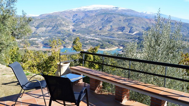 Een terras met tafel en stoelen met uitzicht op een bergachtig landschap met een rivier en een met sneeuw bedekte bergtop.