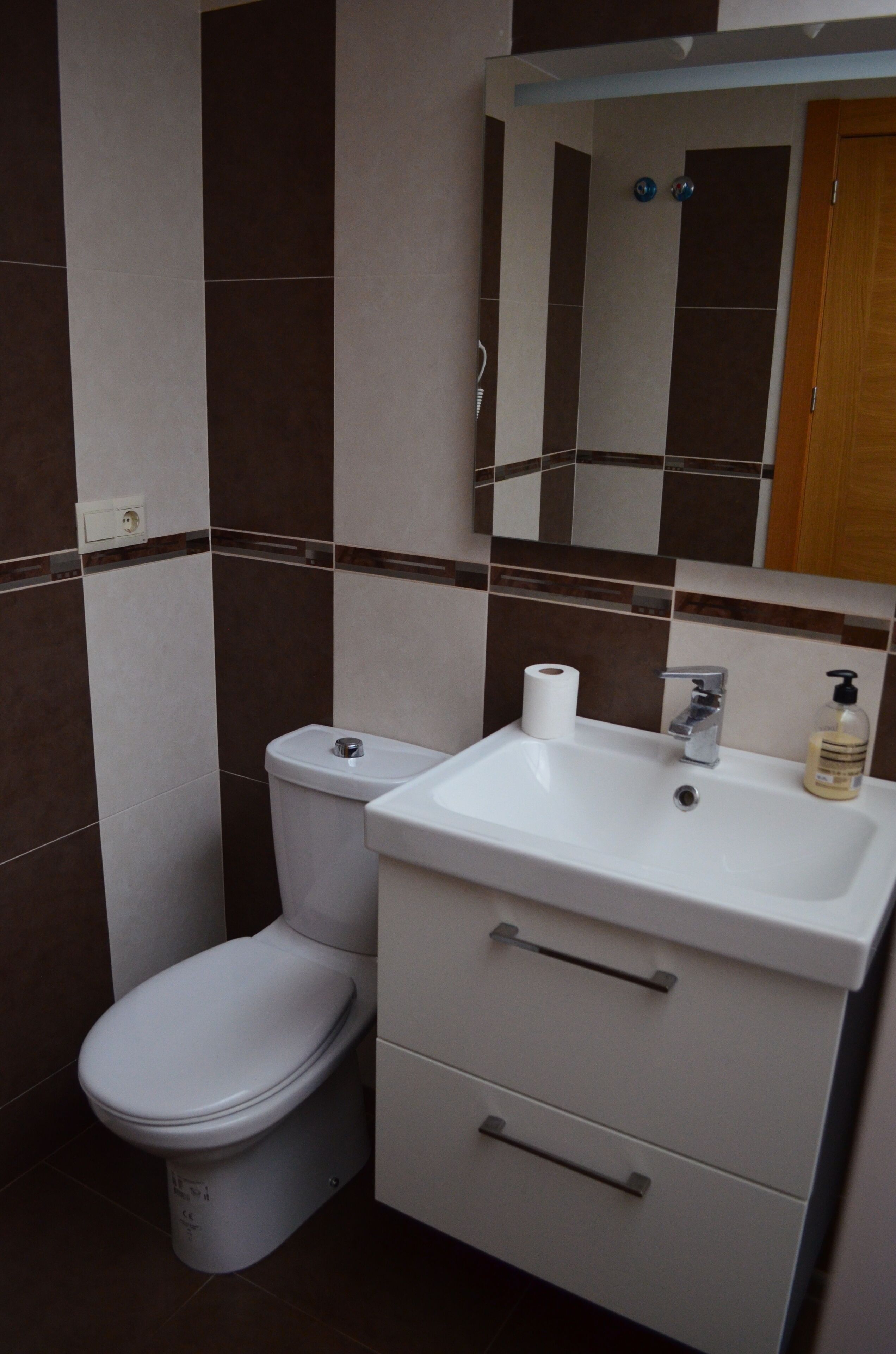 A bathroom with a toilet, sink, mirror, and storage cabinet.