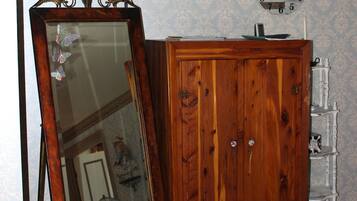 A room with a wooden wardrobe, a large mirror with a decorative frame, a wall clock, and a television mounted on the wall.