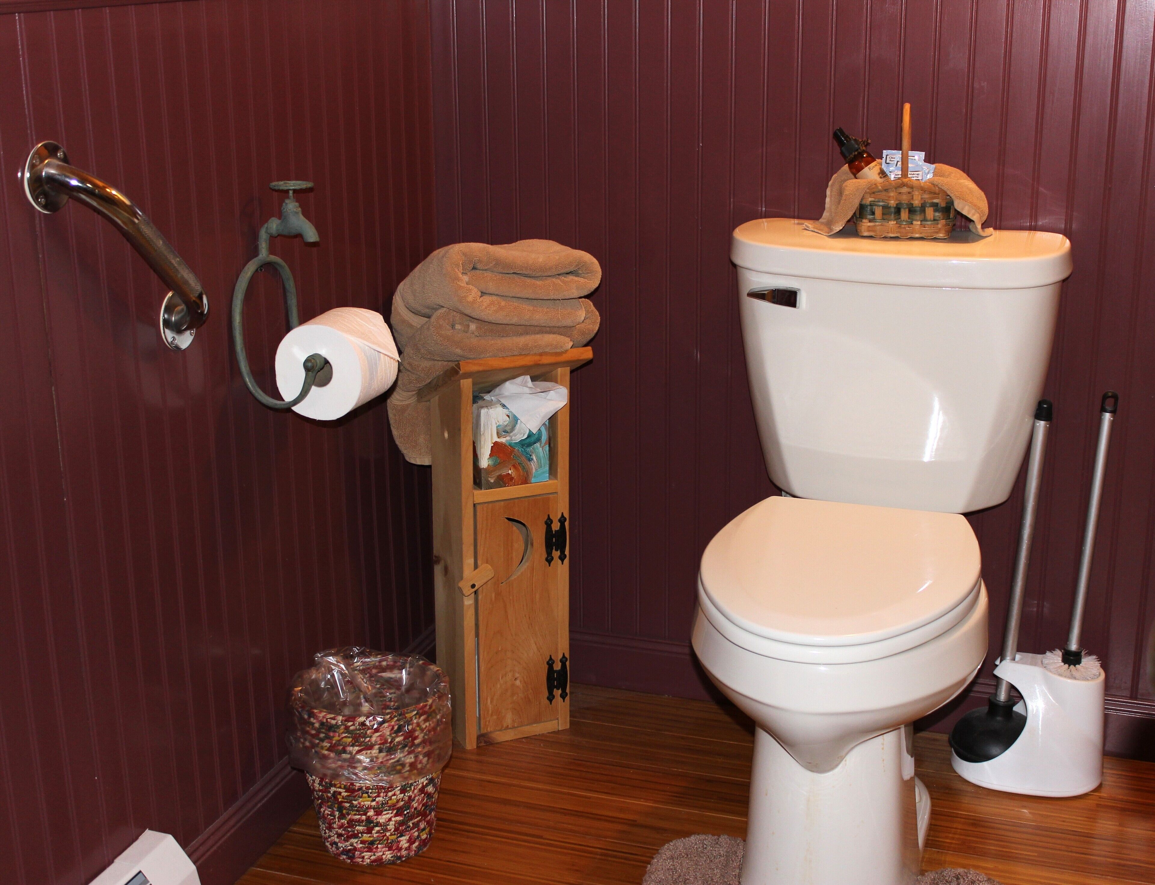 A bathroom with a toilet, a wooden cabinet, a trash bin, and a toilet paper holder.