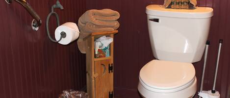 A bathroom with a toilet, a wooden cabinet, a trash bin, and a toilet paper holder.