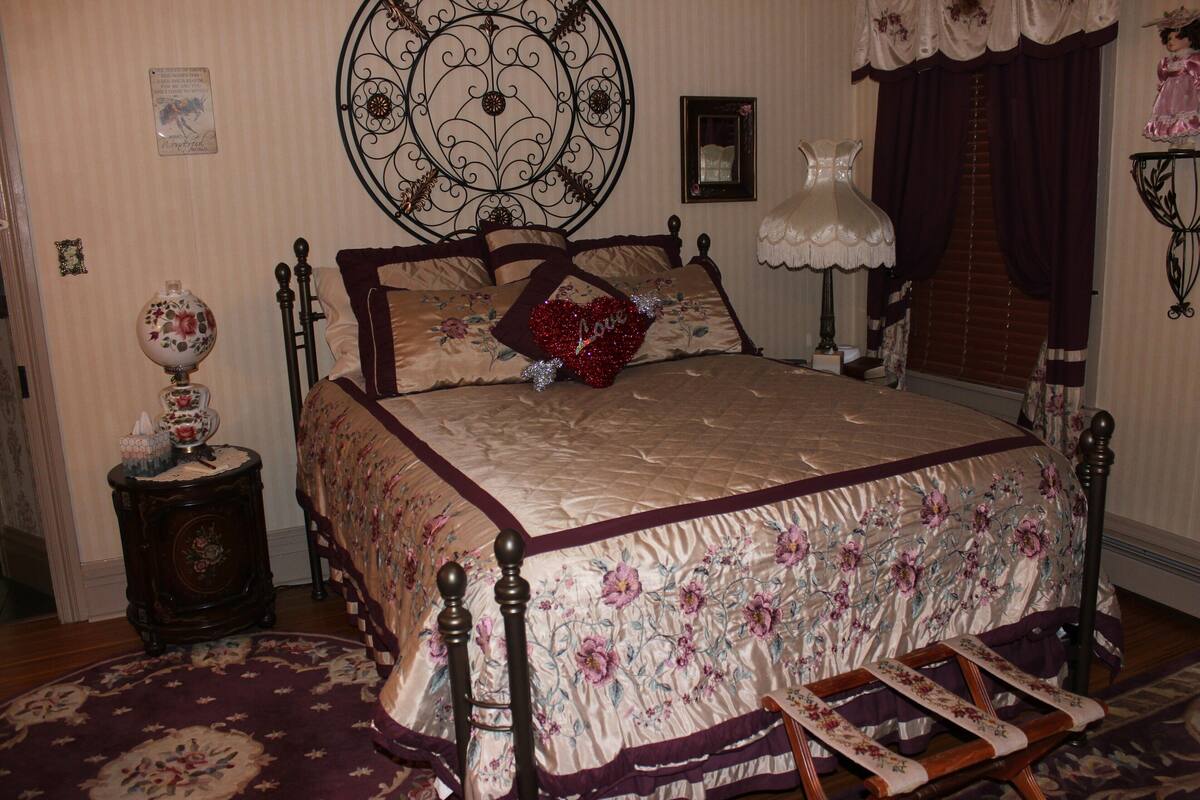 A bedroom with a floral bedspread, a decorative headboard, a bedside table with a lamp, and a nightstand.