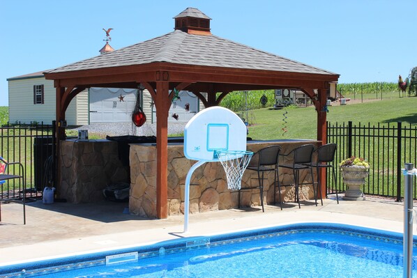 Ett poolområde med en basketkorg, en pergola och en grillplats.