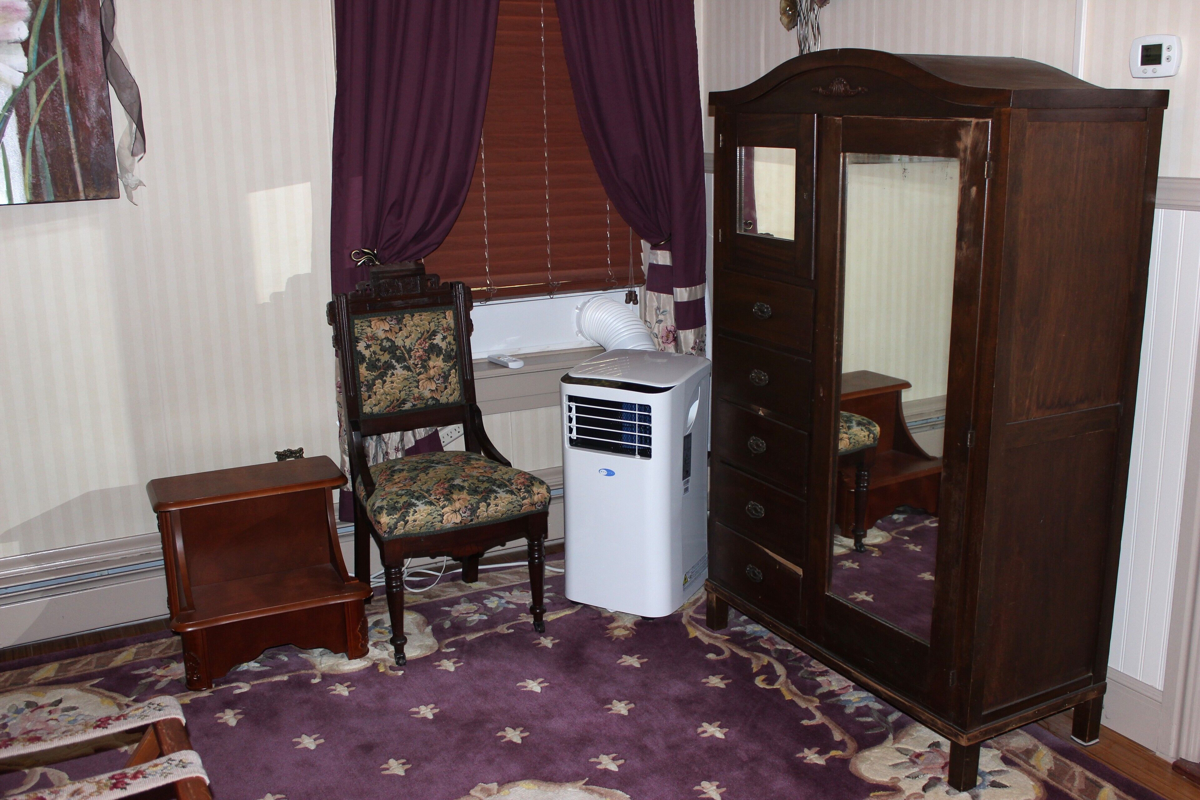 Una stanza con un armadio in legno, una sedia, un tavolino e un termosifone.