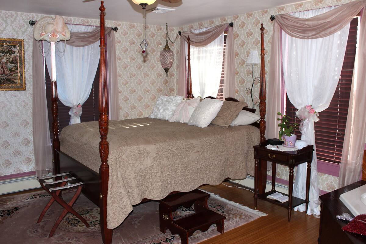 A four-poster bed with a canopy, a bedside table with a lamp, and a small stool.