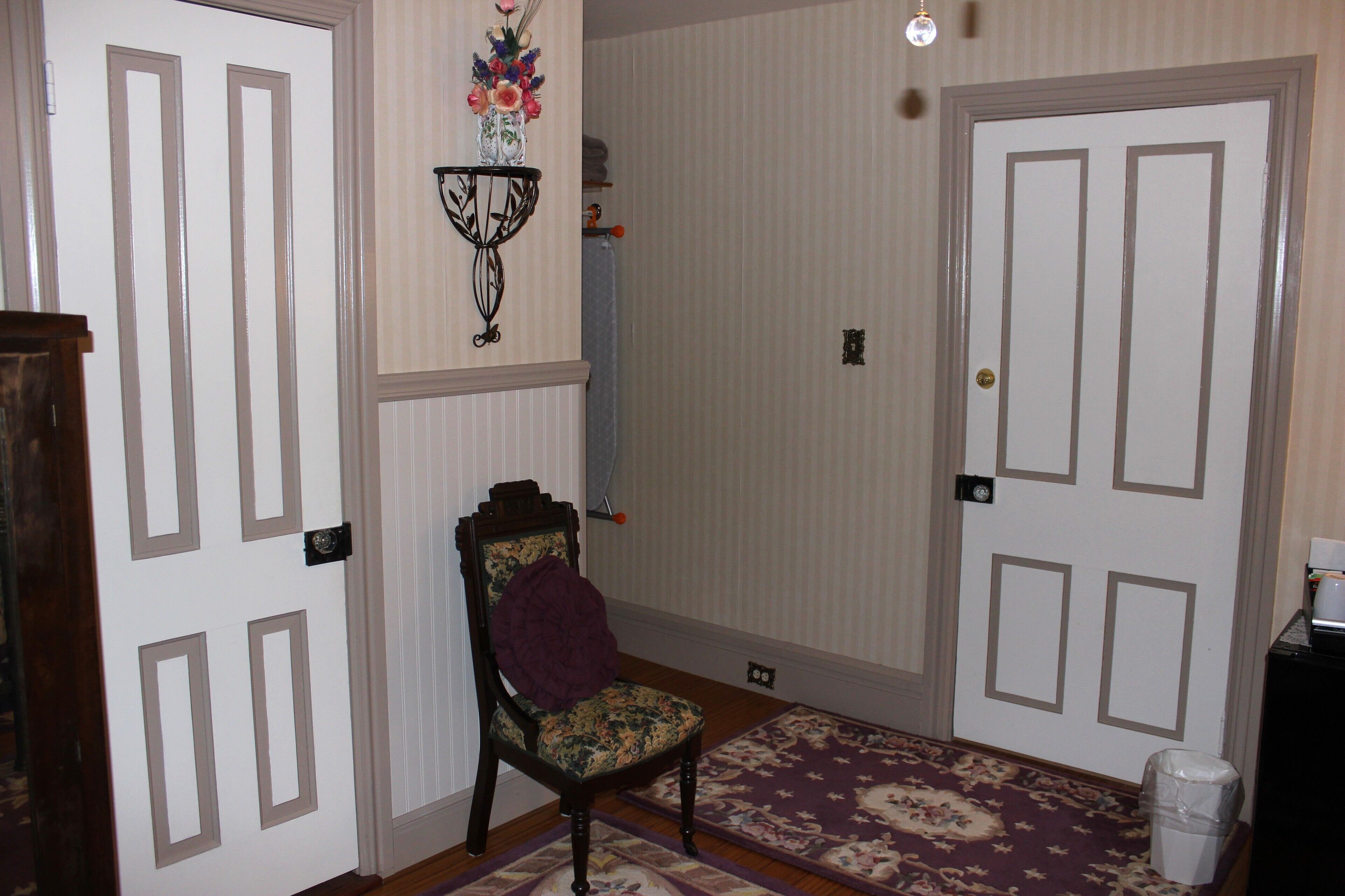 A hallway with a chair, a patterned rug, and two doors.