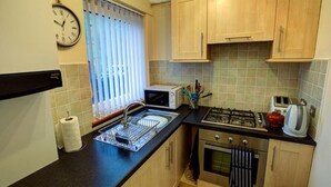 A compact kitchen with a sink, stove, and microwave. - Cedars Apartment (Dunoon)