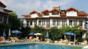 A swimming pool with lounge chairs and umbrellas, surrounded by a building with multiple balconies. - Villa Ozalp Apartments (Ortaca)