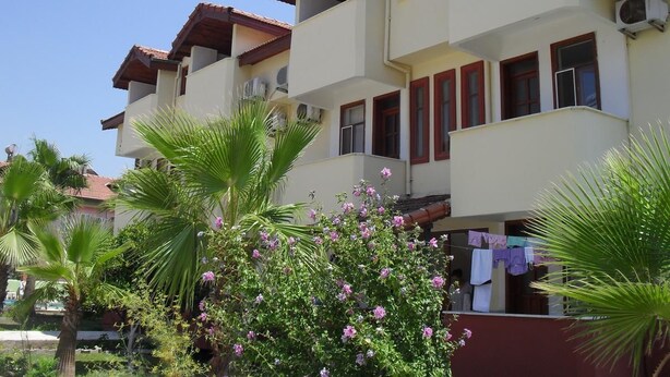 A multi-story building with balconies, air conditioning units, and a garden with palm trees and flowering plants. - Villa Ozalp Apartments (Ortaca)