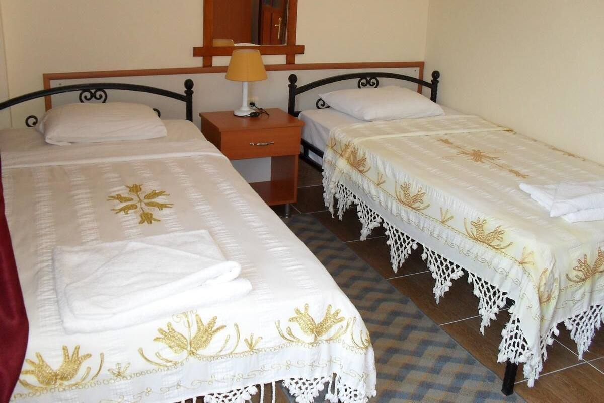 Una habitación con dos camas individuales, una mesita de noche de madera con lámpara y un espejo sobre la cama.
