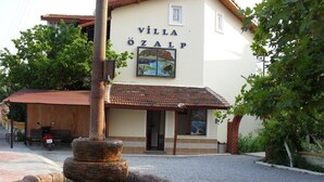 A building named "Villa Ozalp" with a tiled roof, a fountain, and a bench outside. - Villa Ozalp Apartments (Ortaca)