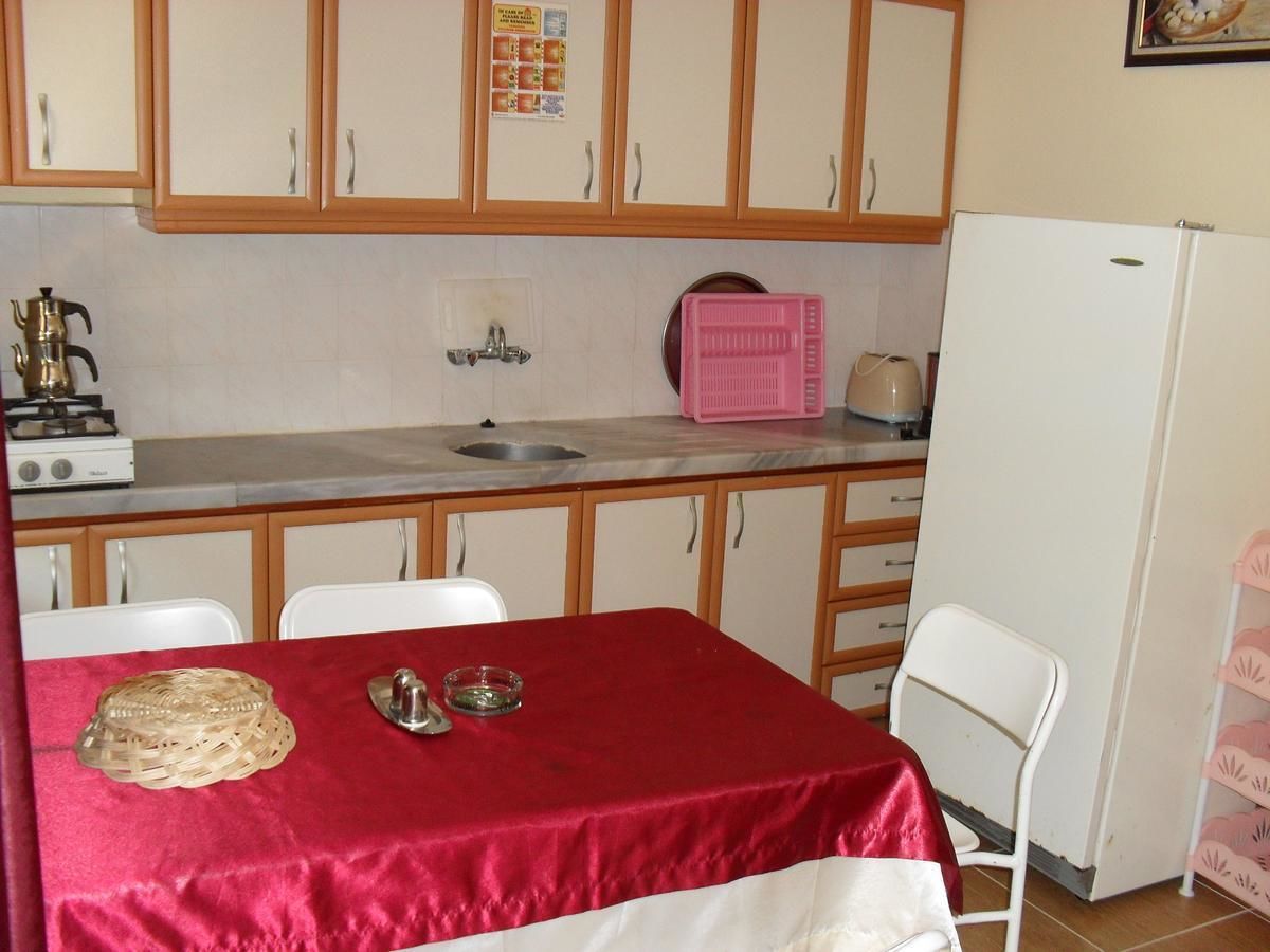 Una cocina con armarios de madera, un fregadero, una estufa y un refrigerador. Hay una mesa con mantel rojo y una cesta.