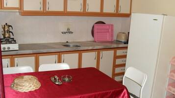 Una cocina con armarios de madera, un fregadero, una estufa y un refrigerador. Hay una mesa con mantel rojo y una cesta.