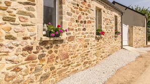 A stone building with three windows, each with a flower box containing pink flowers.