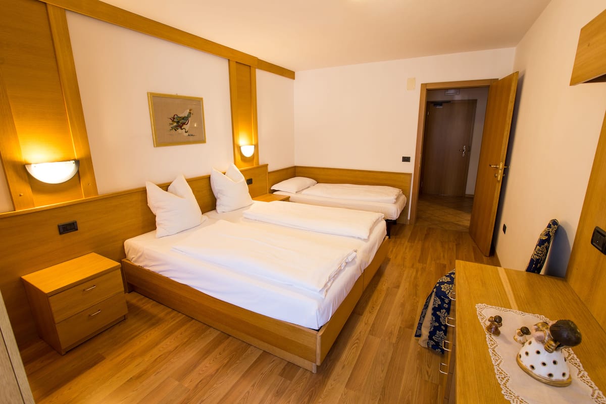A hotel room with a wooden bed, bedside tables, a desk with a chair, and a door leading to another room.