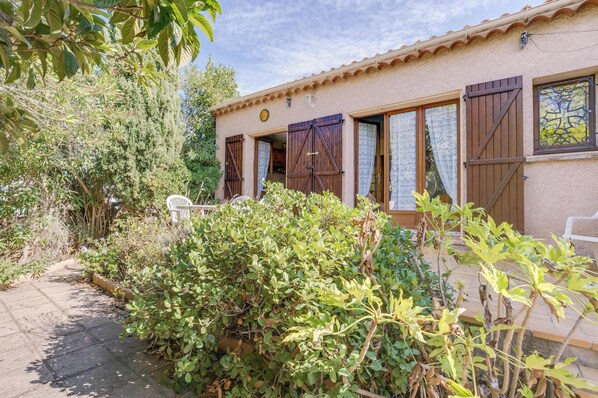 Un bâtiment rustique avec des volets en bois, un toit en tuiles et un jardin agrémenté de différentes plantes.