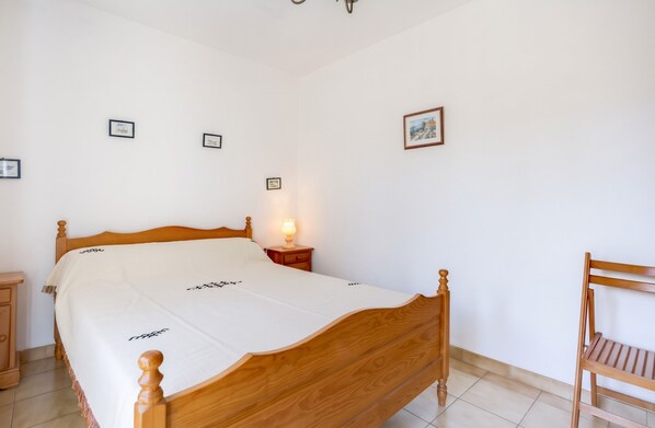 A bedroom with a wooden bed, a nightstand with a lamp, and a chair. - Homerez - House in Agde (Agde)