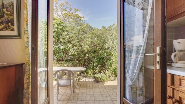Eine offene Schiebetür führt auf eine Terrasse mit Tisch und Stühlen, umgeben von viel Grün.