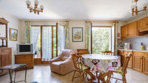 Ein gemütliches Wohnzimmer mit einer Couch, einem Esstisch mit Stühlen, einem Fernseher auf einer Holzkommode und einer Küchenzeile mit Holdekor und gefliestem Fliesenspiegel.