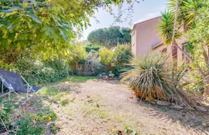 A garden with a variety of plants, a patio area, and a building with a beige facade. - Homerez - House in Agde (Agde)