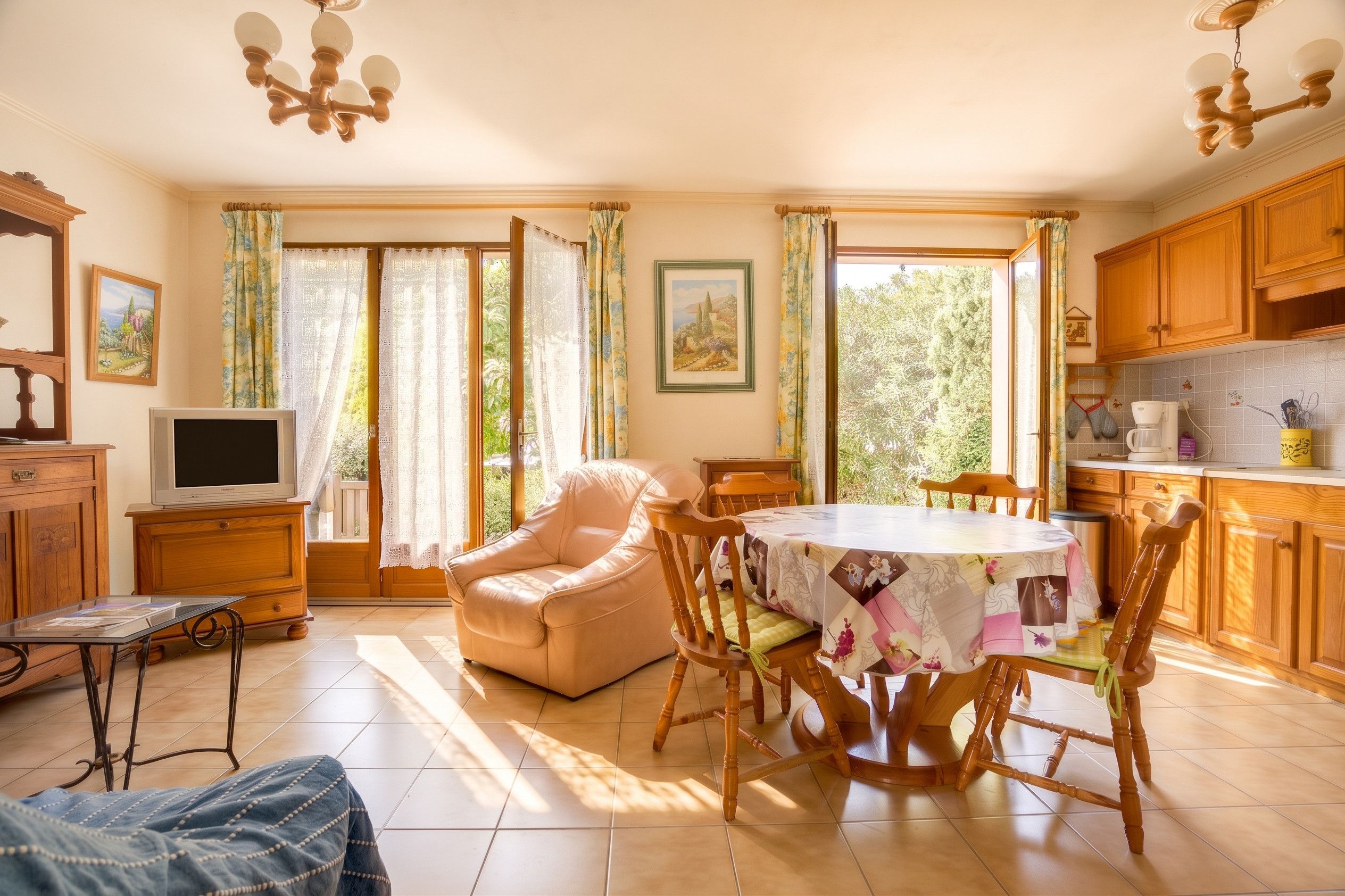 A cozy living room with a sofa, a dining table with chairs, a television, and a kitchen area with wooden cabinets and a coffee maker.