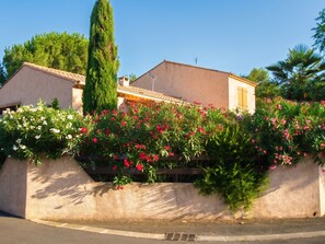 A residential building with a beige facade, a tiled roof, and a garden with flowering plants.