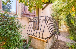 A balcony with a wrought iron railing, surrounded by greenery and a building with a textured wall. - Homerez - House in Agde (Agde)
