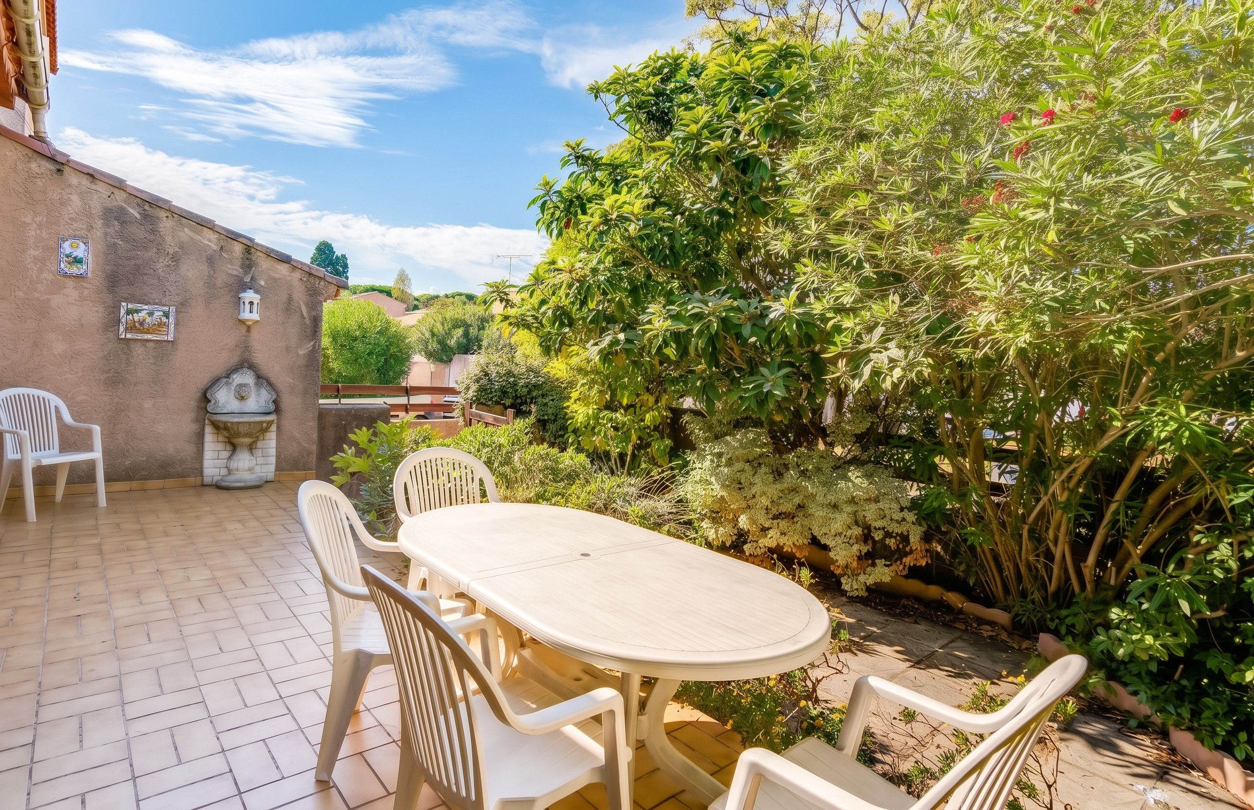 A patio with a round table and chairs, surrounded by lush greenery and a brick wall.