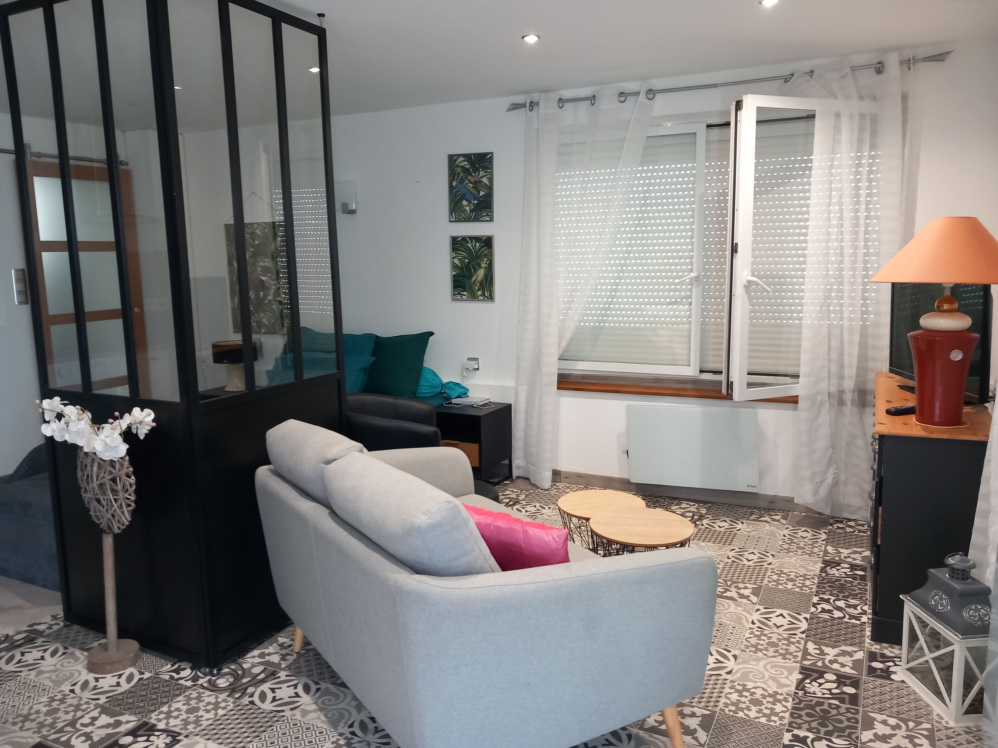 A modern living room with a sofa, a small table, a lamp, and a window with blinds.