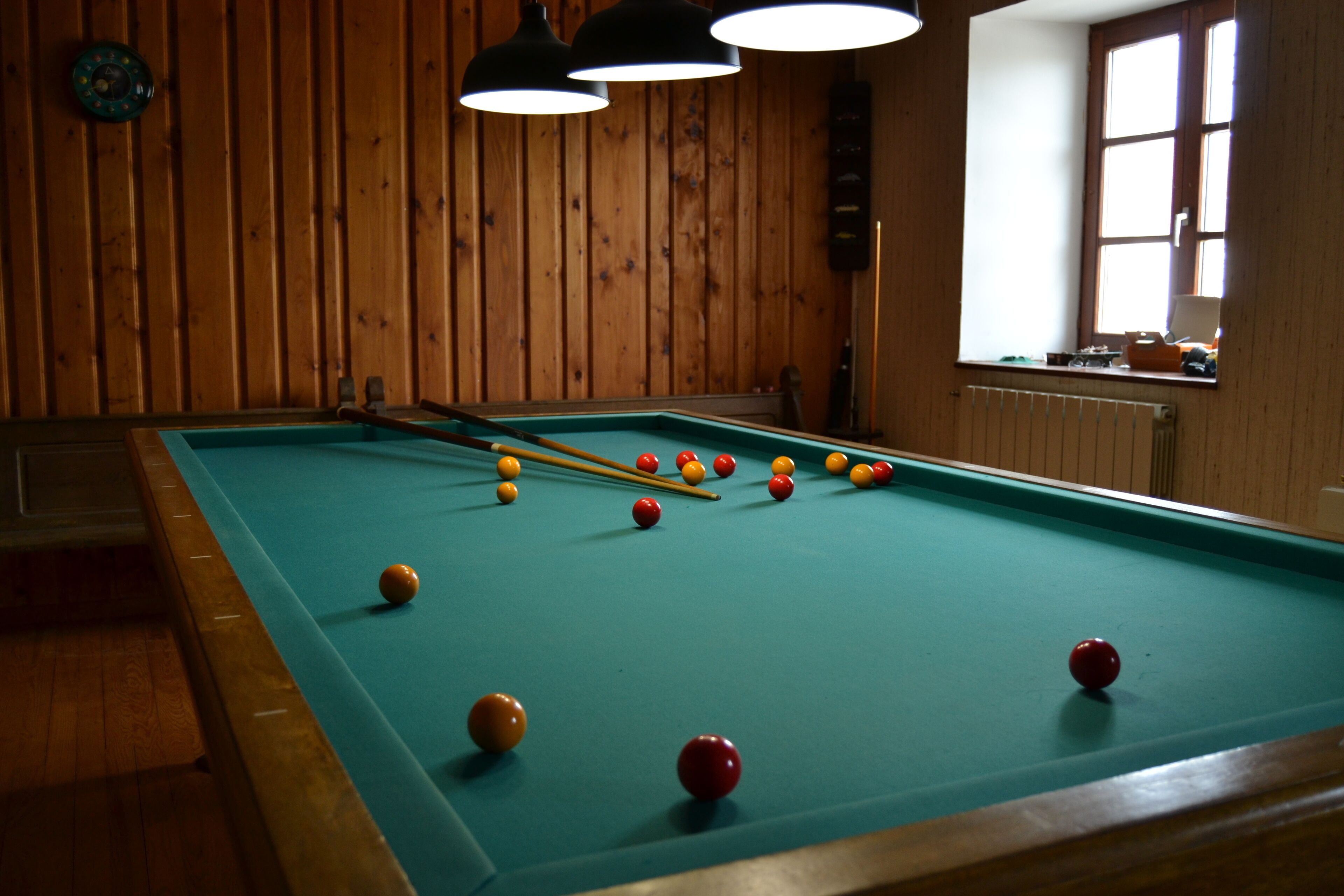 A pool table with balls, wooden walls, and hanging lights.