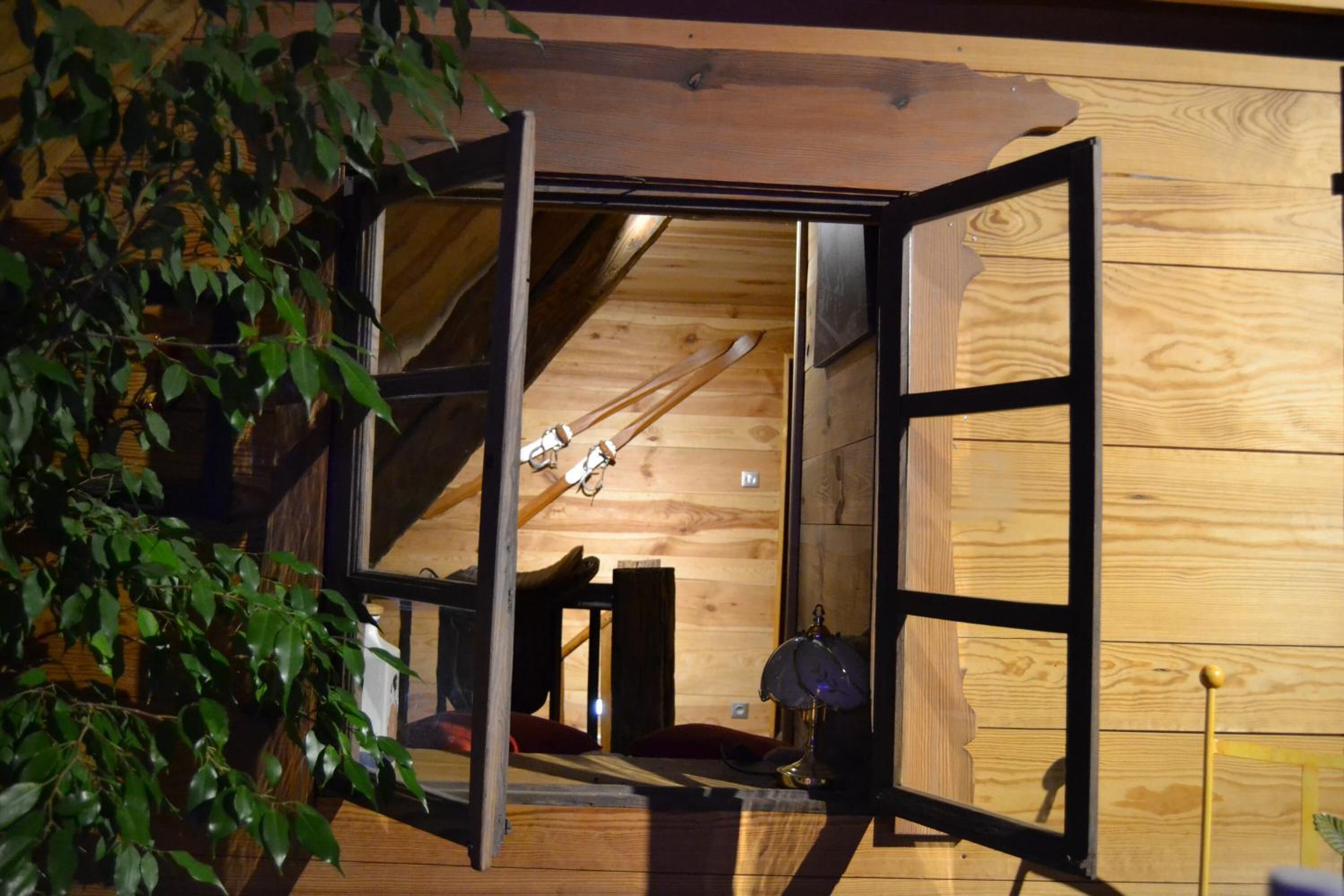 Interior de madera con un amplio ventanal que da a una habitación con esquíes y una lámpara.