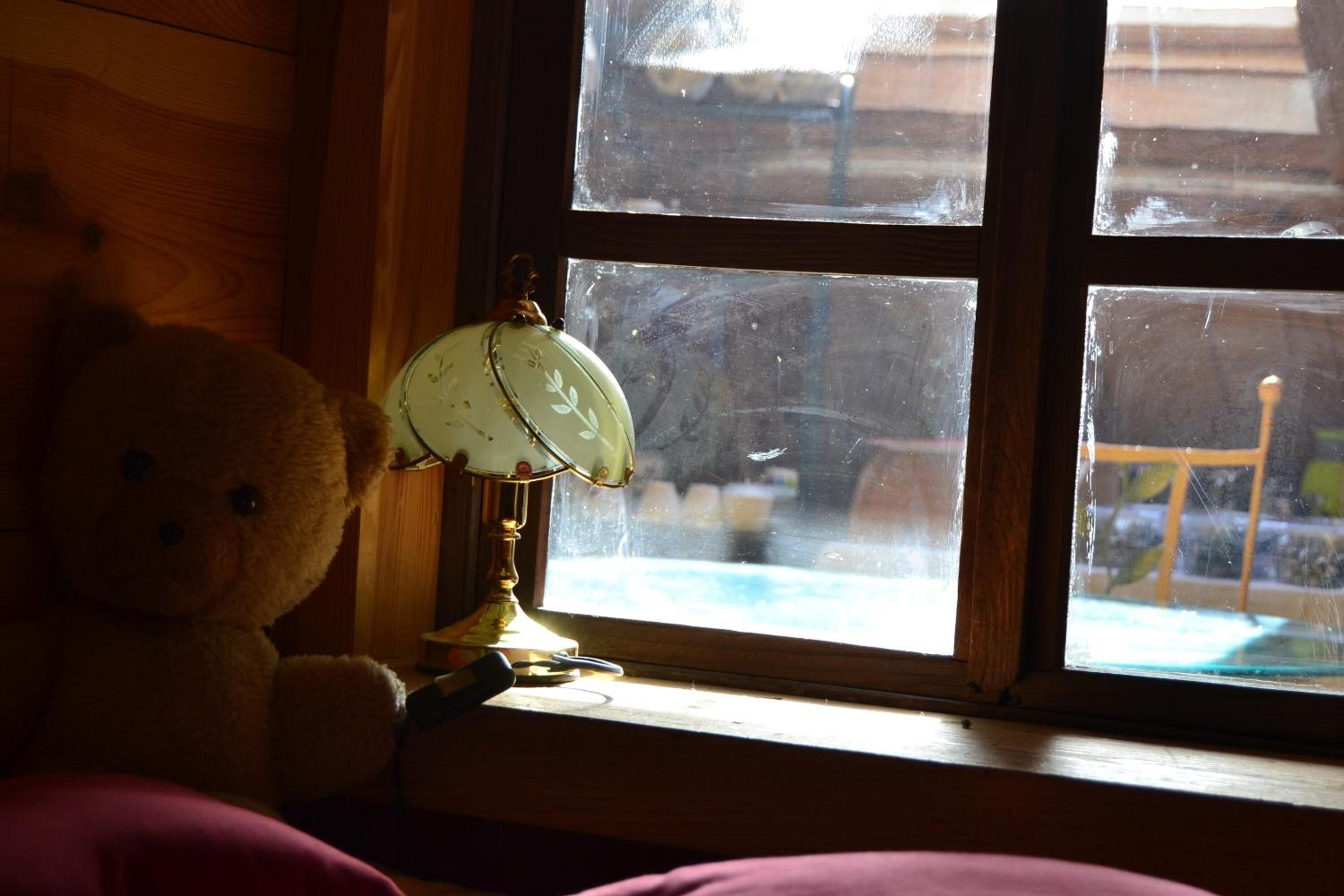 A window with a teddy bear and a lamp on a wooden ledge.