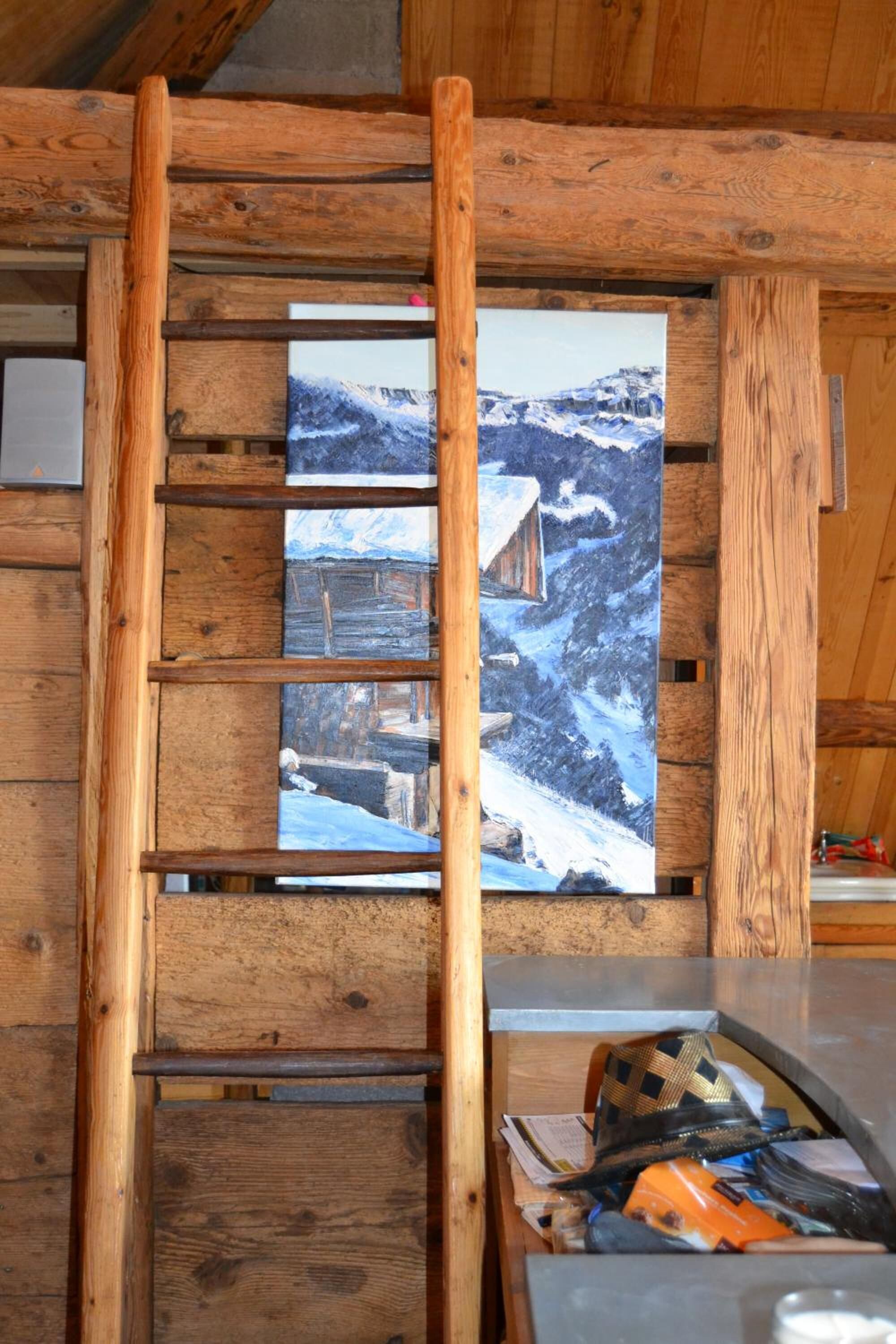 A wooden cabin interior with a wooden ladder leading to a window displaying a snowy mountain scene.