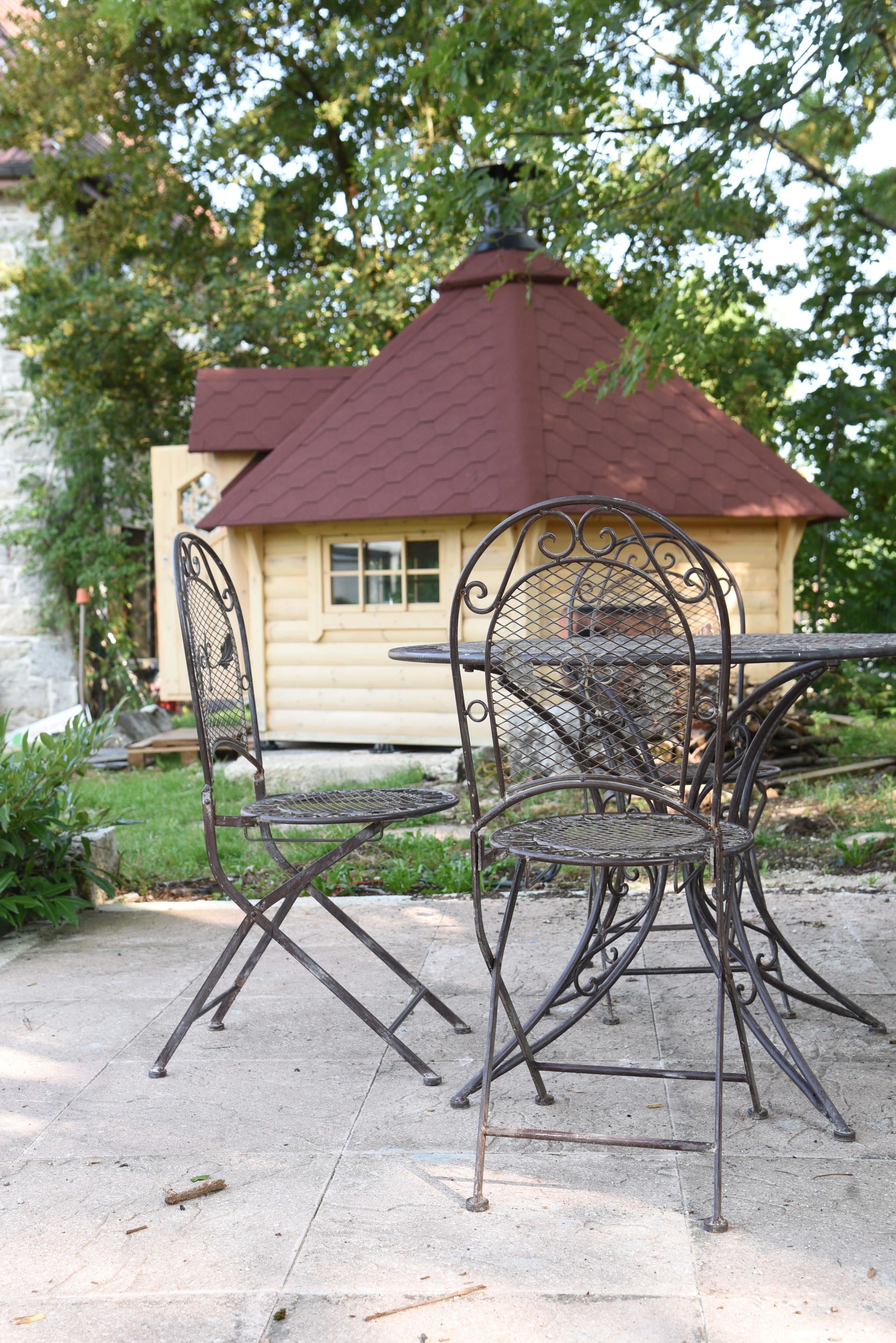 A metal outdoor table and chairs with a wooden house in the background.