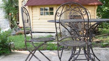 A metal outdoor table and chairs with a wooden house in the background.