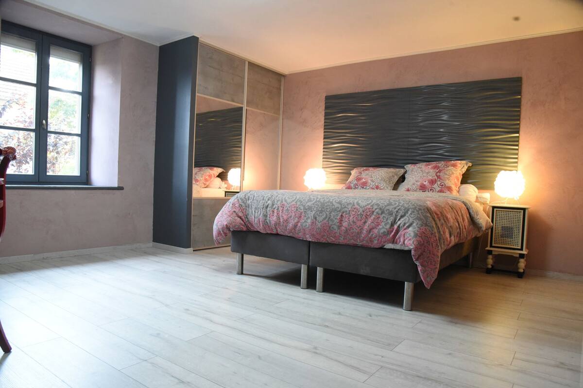 A bedroom with a bed, bedside lamps, a window, and a mirror.