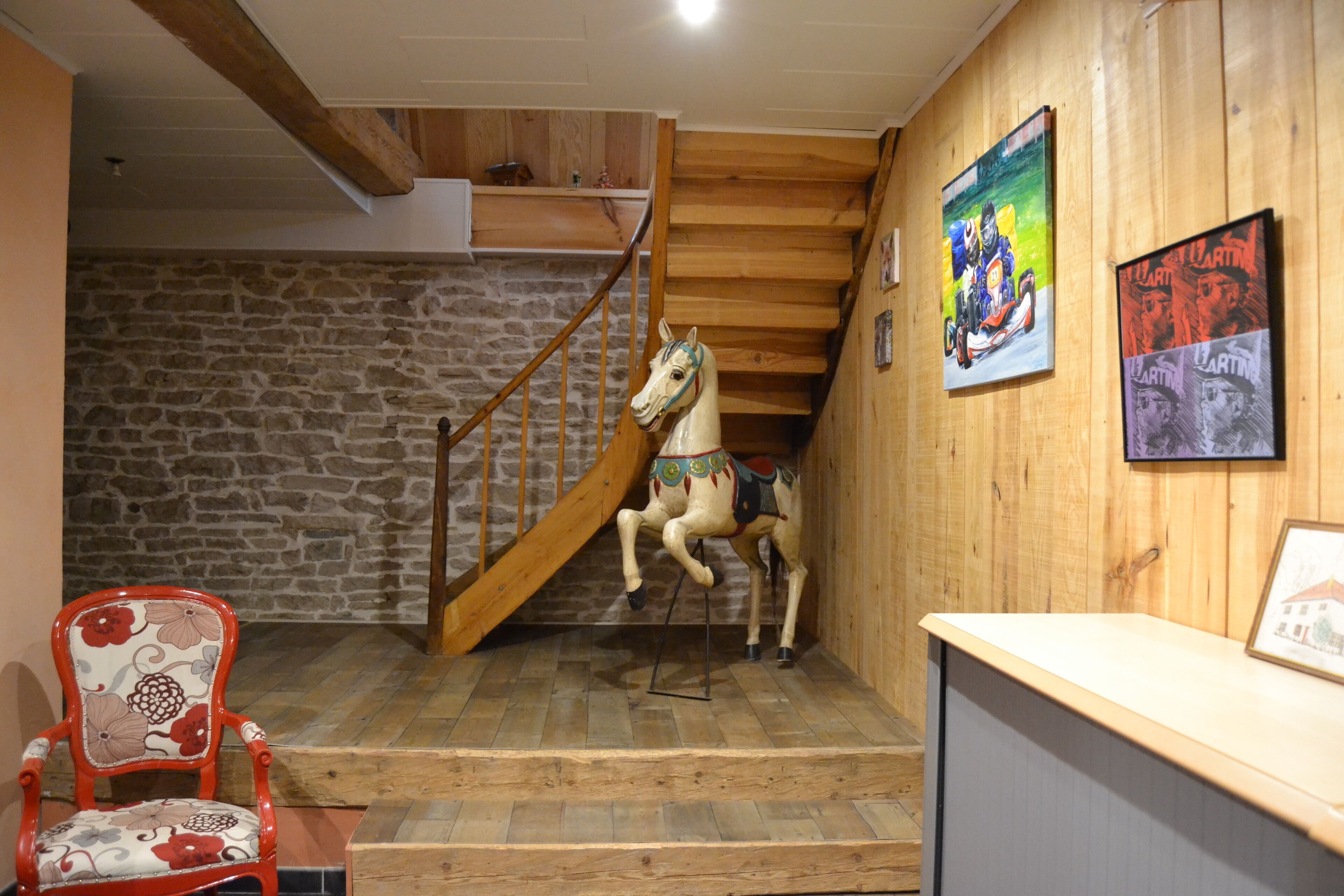 A wooden staircase with a carousel horse, a red chair, and two framed pictures on the wall.