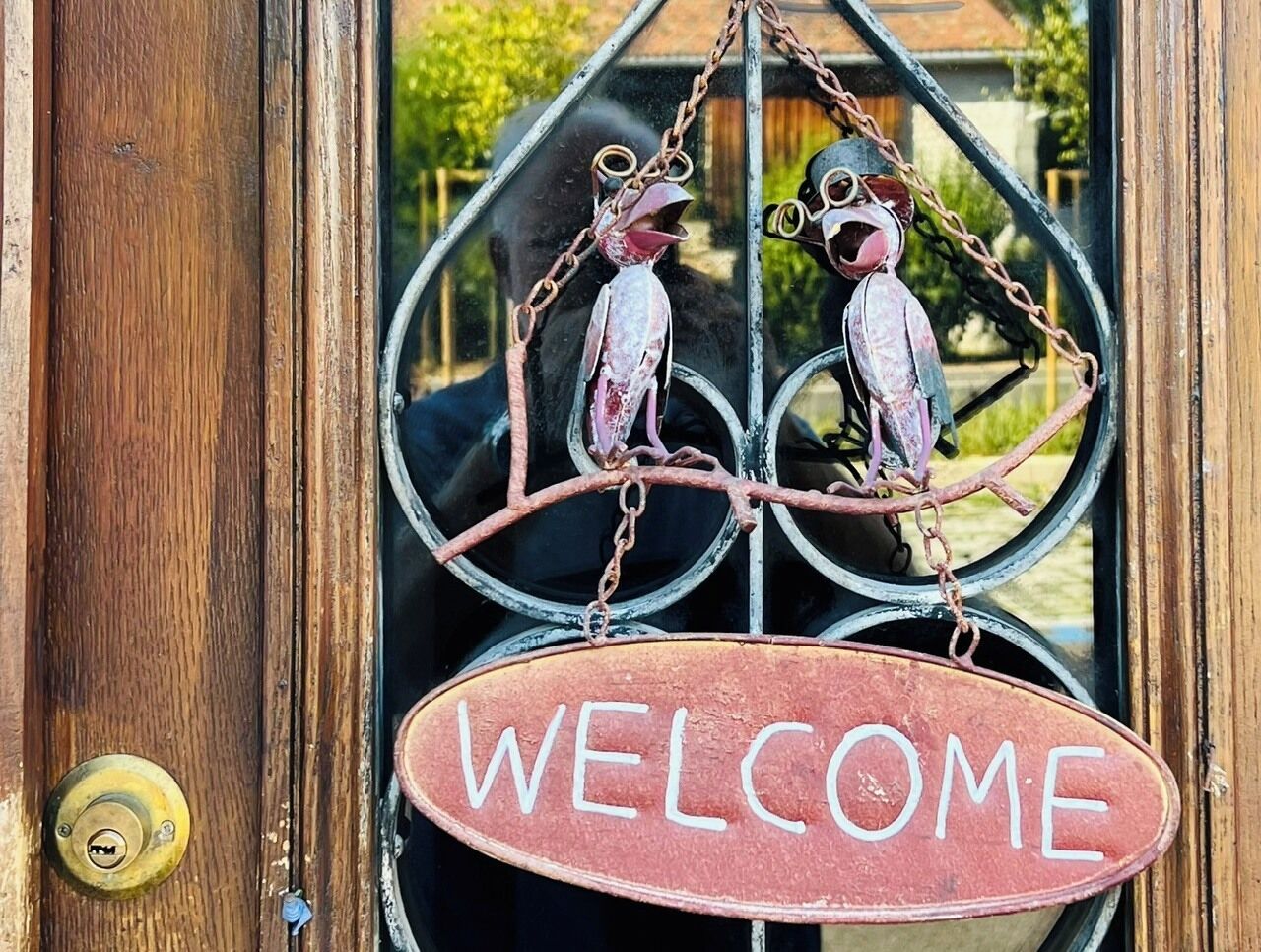A wooden door with a brass doorknob and a metal sign that reads 'WELCOME' above a decorative metal birdcage.
