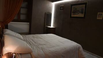 Une chambre à coucher avec un lit, une table de chevet, une lampe, une fenêtre avec des rideaux et des tableaux encadrés accrochés au mur.