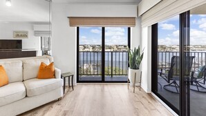 A modern living room with a sofa, a small table, and a large window with a view of a body of water and buildings.