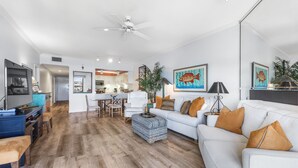 A modern living room with a white sofa, wooden flooring, and a ceiling fan.